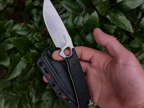 Hand holding folding knife against green foliage background