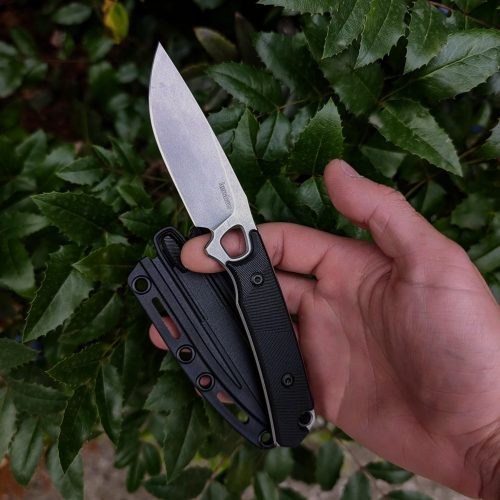 Hand holding folding knife against green foliage background